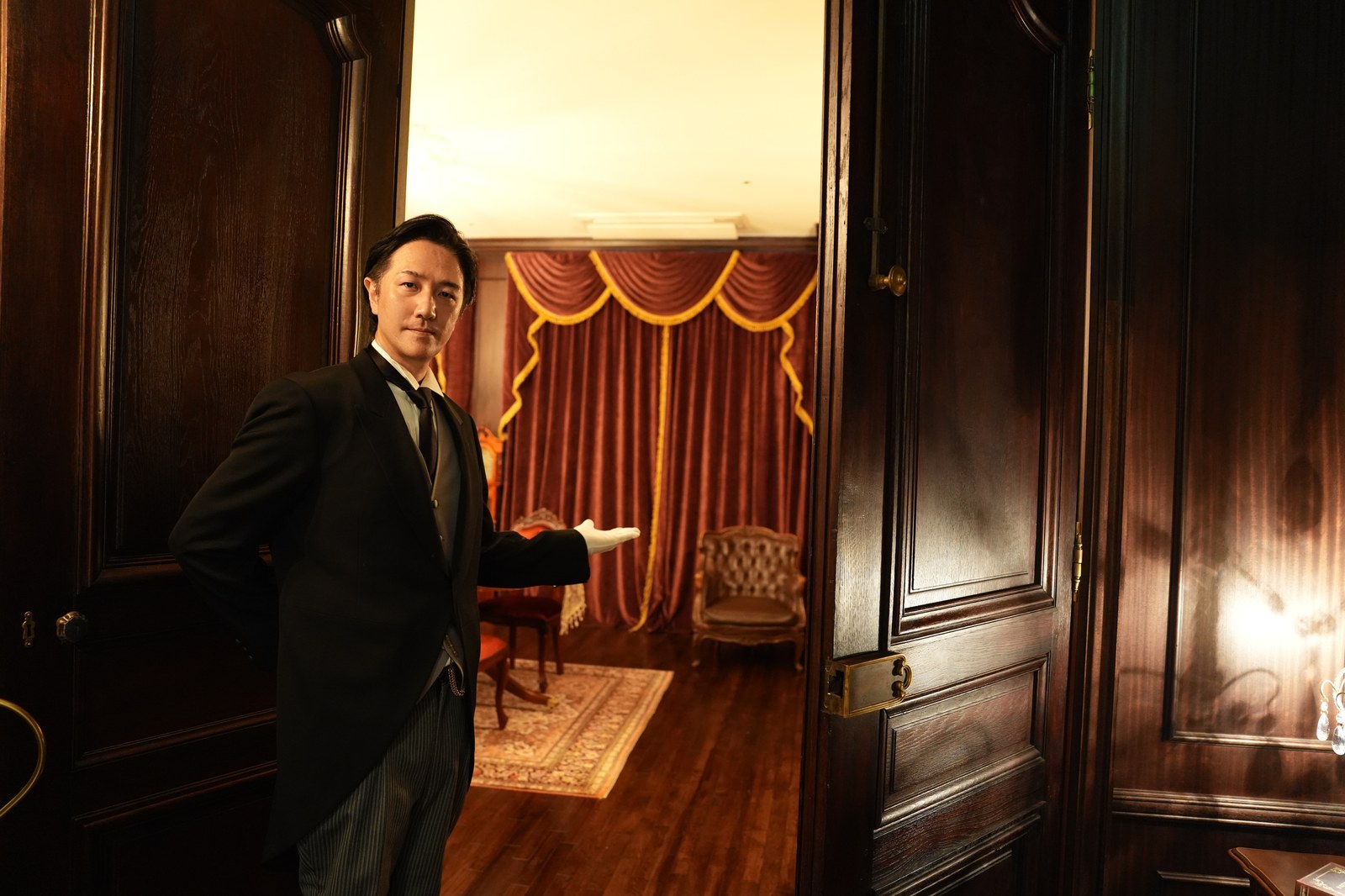 Footman service. A butler opening a door and gesturing into a formal reception room for guest arrival support