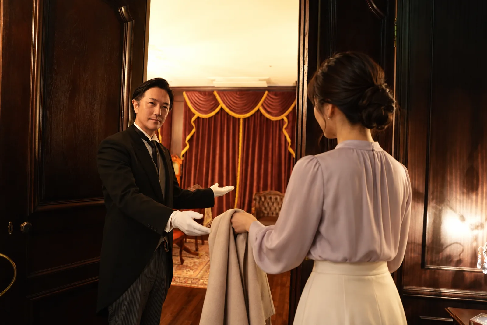 A butler welcoming a guest at the door of the mansion